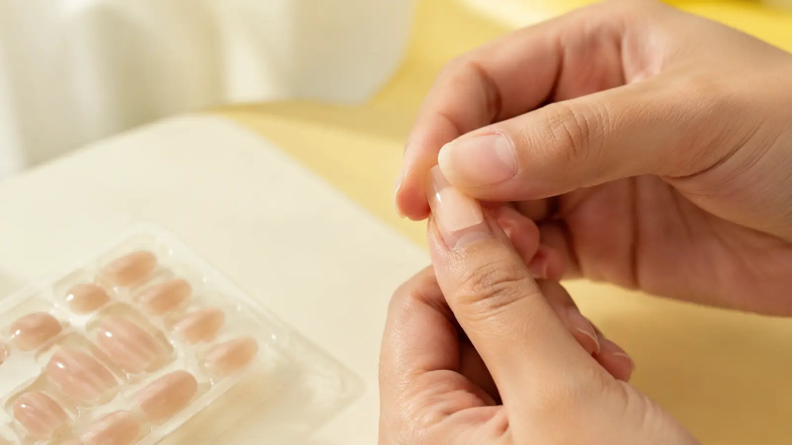 Dry-fitting a short nude press-on nail over a clean natural thumbnail before adhesive.