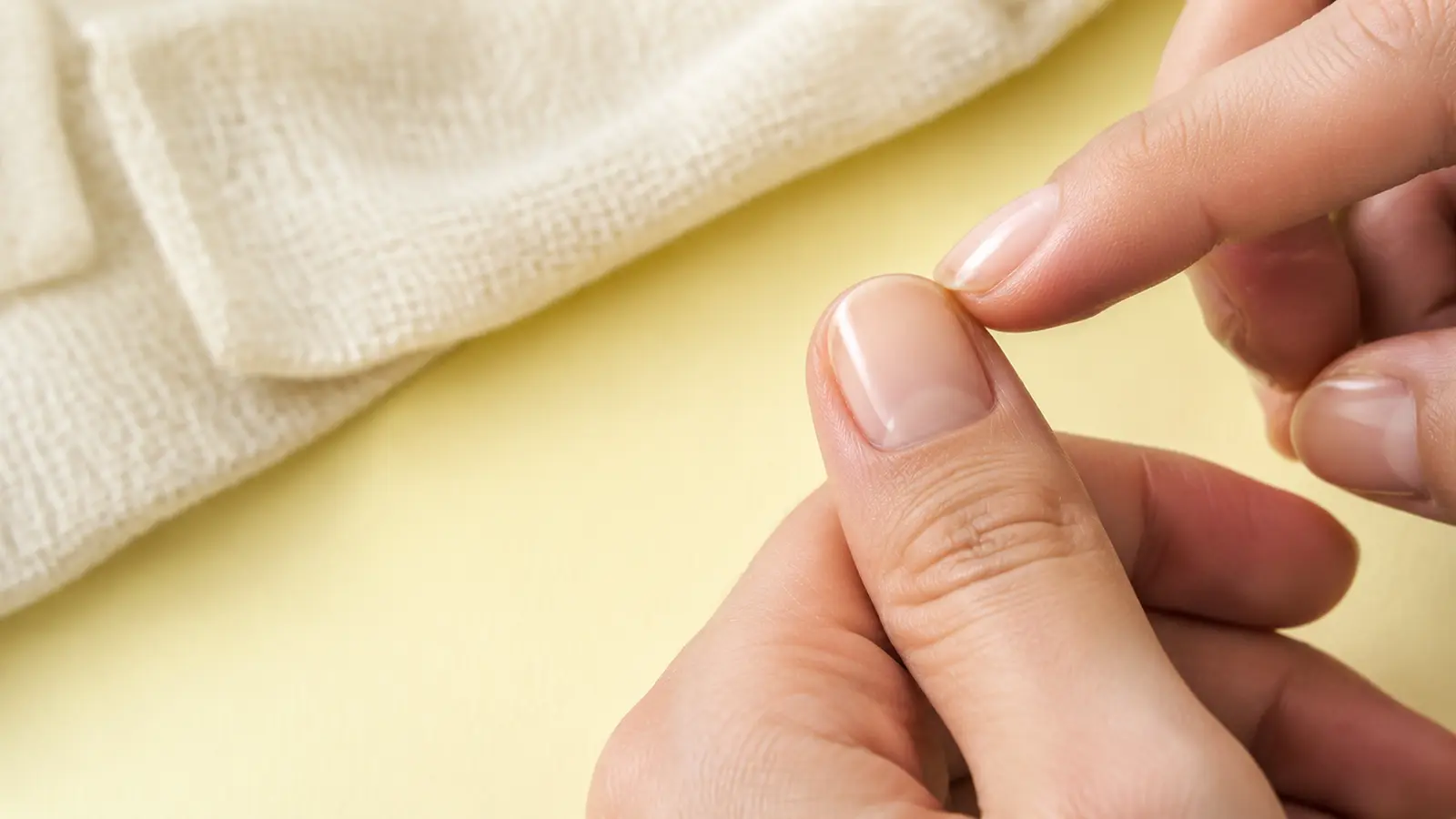 A short nude press-on sitting flush on a natural thumbnail while its sidewall alignment is checked during a dry fit.