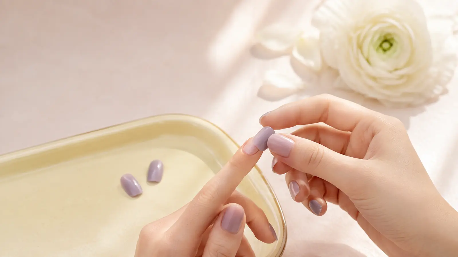 Dry-fitting a short lavender press-on over a natural nail to check that both sidewalls make contact before adhesive.